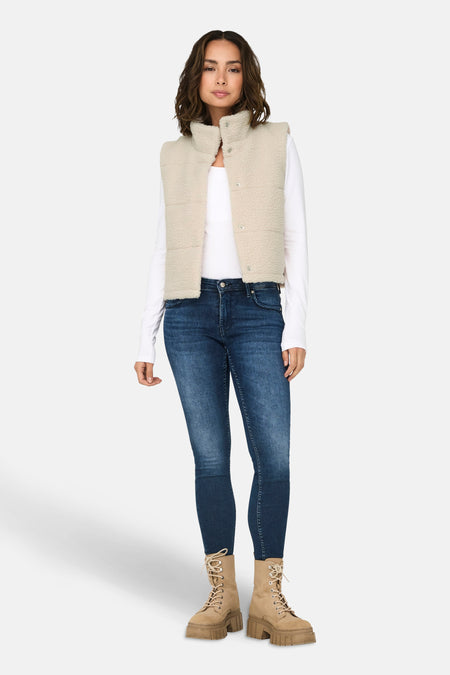 Veste sans manches écru de ONLY, portée avec un jean bleu et des bottes à lacets beiges.
