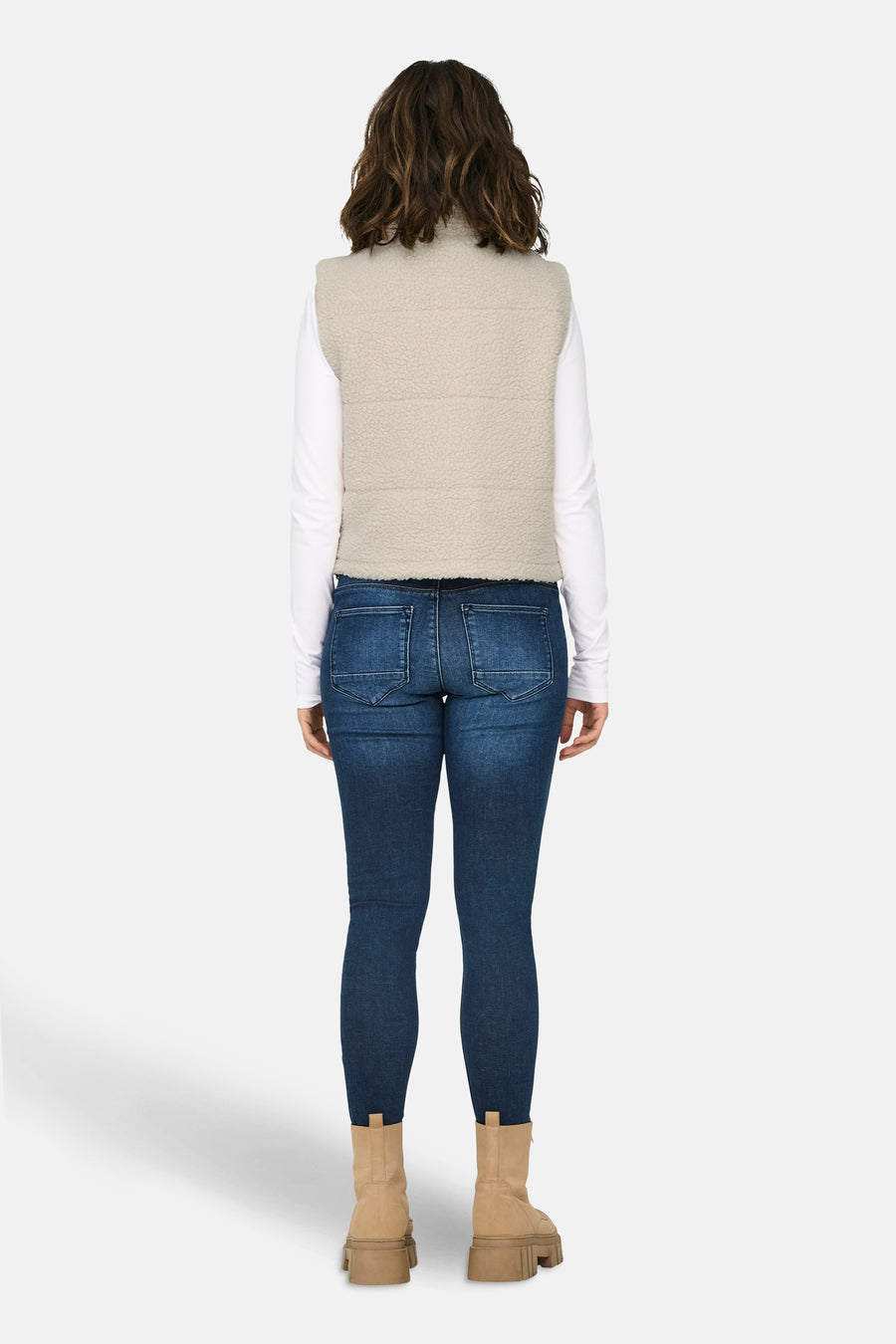 Veste sans manches écru de ONLY, portée sur un haut blanc à manches longues, avec un jean bleu et des bottes beige.