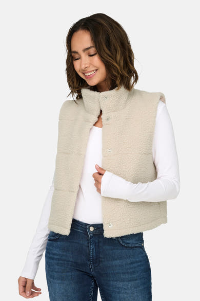 Veste sans manches écru de ONLY, portée sur un t-shirt blanc à manches longues et un jean bleu.