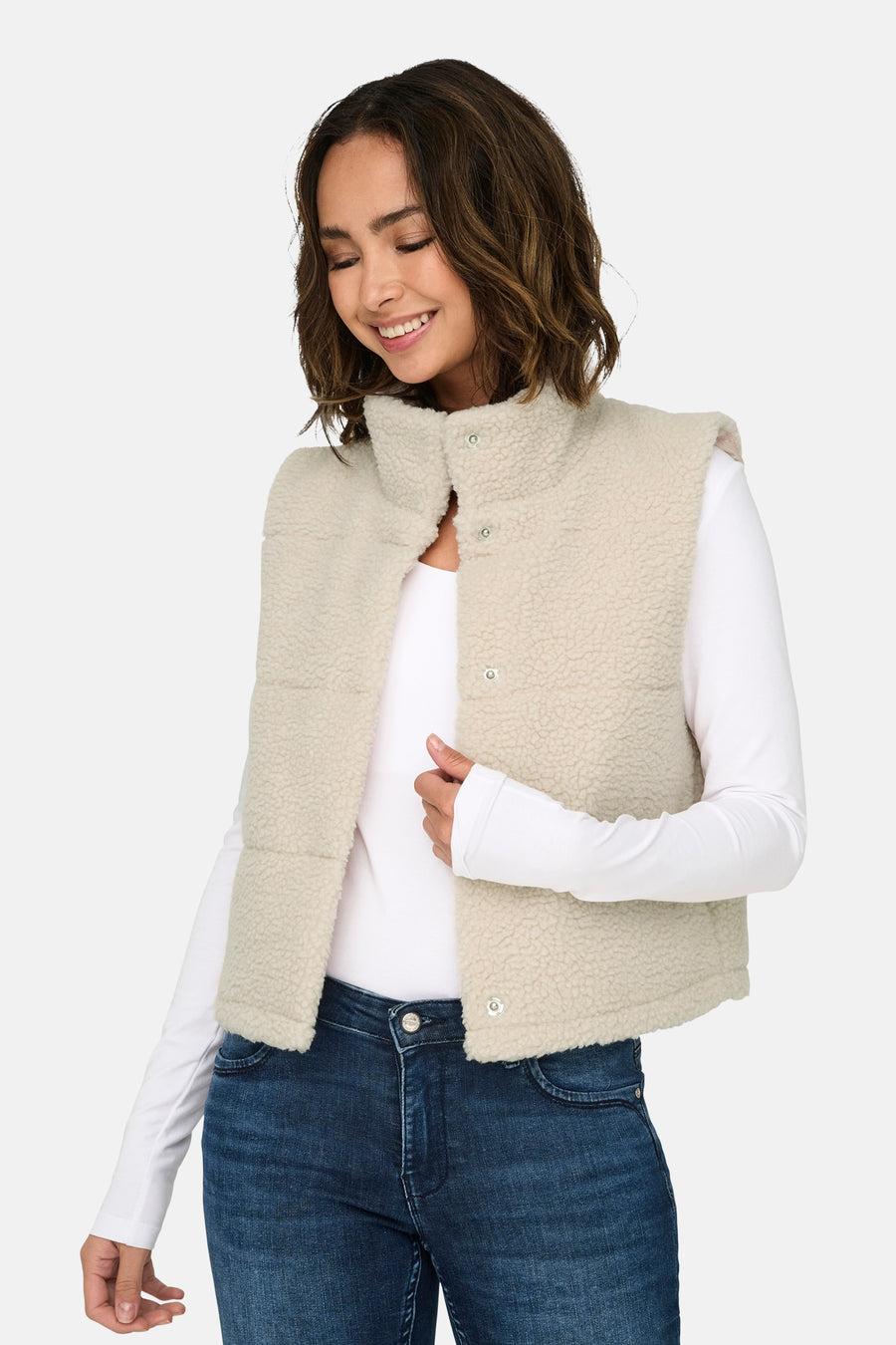 Veste sans manches écru de ONLY, portée sur un t-shirt blanc à manches longues et un jean bleu.