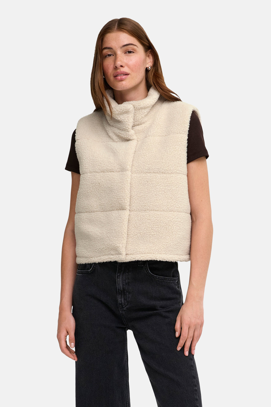 Cream shearling bodywarmer with turtleneck and quilted panels, worn over a dark brown short-sleeve top and black jeans, front view.