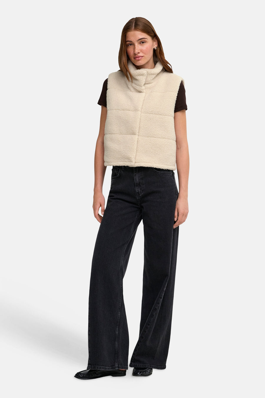 Cream shearling bodywarmer with turtleneck and quilted panels, worn over a dark top with wide-leg jeans and black loafers, front view.