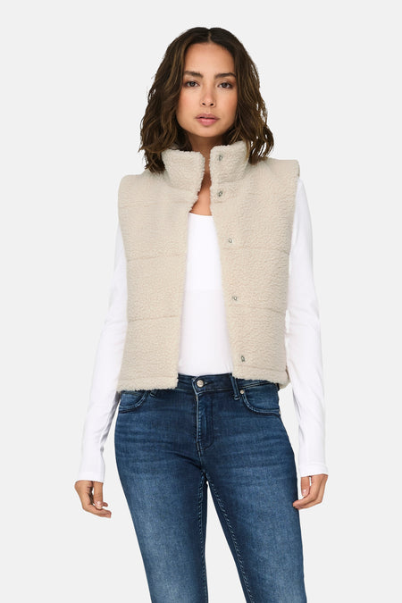 Veste sans manches écru de ONLY, portée sur un haut blanc à manches longues et un jean bleu.