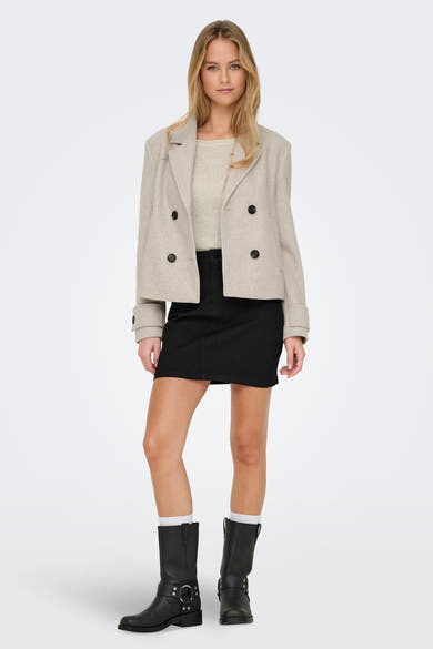 Korte beige jas van ONLY, gedragen met een zwarte minirok en rijlaarzen.