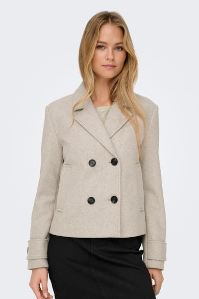Korte beige jas van ONLY, dubbele rij knopen met zwarte knopen, gedragen over een effen zwarte broek.