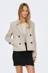 Korte beige jas van ONLY, met zwarte dubbele knoopsluiting, gedragen met een crèmekleurige top en een zwarte minirok.