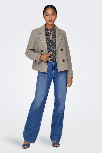 Veste courte beige par ONLY, avec une chemise à motif et un jean taille haute porté avec une ceinture.
