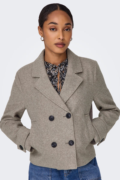 Veste courte beige de ONLY, portée sur un chemisier à motifs, avec un jean visible.
