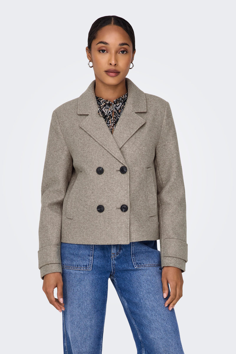 Veste courte beige de ONLY, avec double boutonnage et poches apparentes, portée sur un chemisier à motifs et un jean bleu.