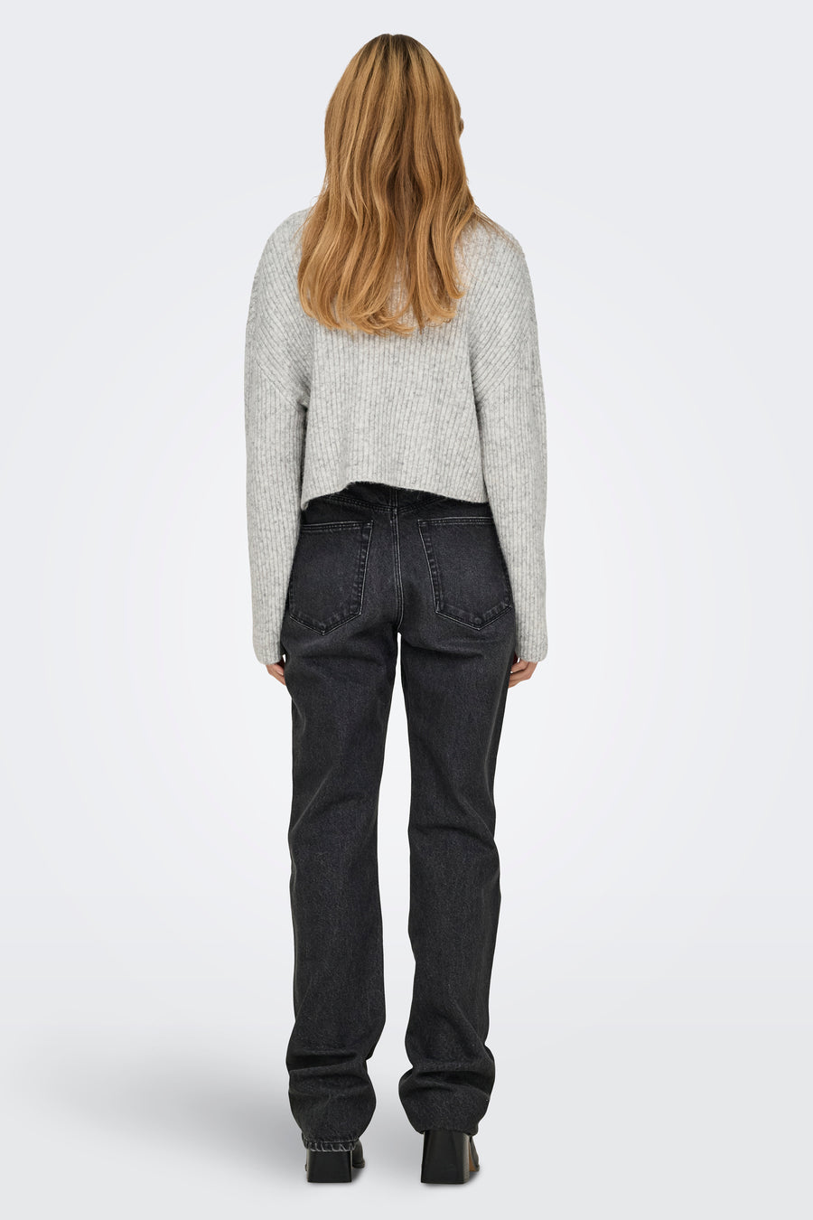 Grijze coltrui van ONLY, gedragen met een zwarte broek en zwarte hakken, van achteren gezien.