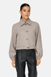 Veste courte beige de ONLY, avec col classique et boutons, portée avec un pantalon en cuir noir.
