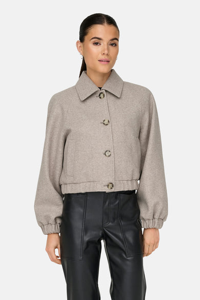 Veste courte beige de ONLY, avec col classique et boutons, portée avec un pantalon en cuir noir.
