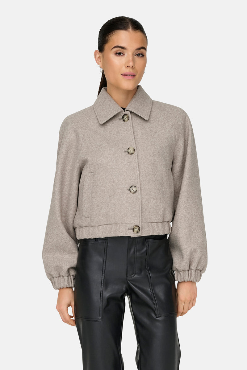 Veste courte beige de ONLY, avec col classique et boutons, portée avec un pantalon en cuir noir.
