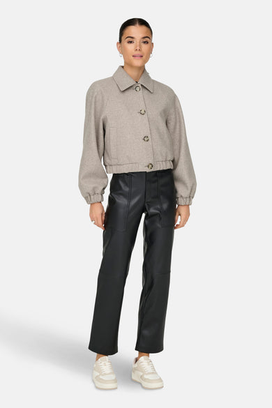 Veste courte beige de ONLY, avec des manches bouffantes et des boutons, portée avec un pantalon noir et des baskets blanches.
