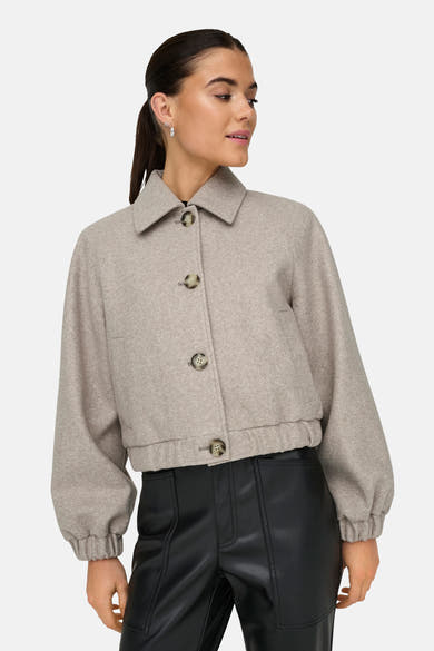 Veste courte beige de ONLY, avec des boutons, portée avec un pantalon noir.
