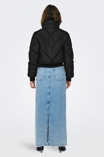 Veste courte noire de ONLY, avec matelassage à chevrons, portée avec une longue jupe en jean.