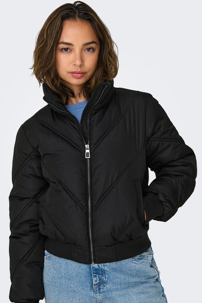 Veste courte noire par ONLY, matelassée avec une fermeture éclair argentée, portée sur un pull bleu et un jean.