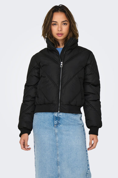 Veste courte noire de ONLY, matelassée avec fermeture éclair argentée, portée sur une jupe en jean bleu.