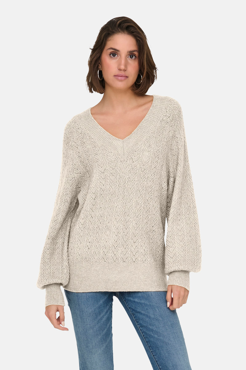 Pull à col en V écru de ONLY, avec une texture tricotée et porté avec un jean bleu.