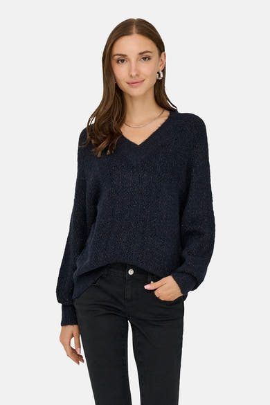 Pull bleu à col en V de ONLY®, porté avec un pantalon noir et des bijoux argentés.
