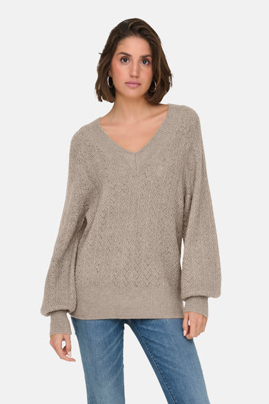 Pull beige à col en V de ONLY, avec motif ajouré et manches bouffantes, porté avec un jean.
