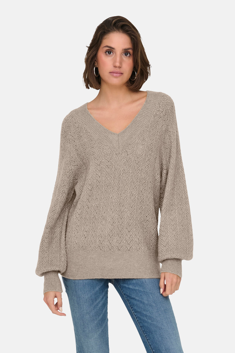 Pull beige à col en V de ONLY, avec motif ajouré et manches bouffantes, porté avec un jean.
