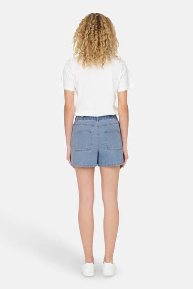 Short en denim bleu clair de JDY, avec poches arrière et taille élastique, porté avec un t-shirt blanc et des baskets.