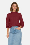 Pull à col roulé bordeaux de ONLY®, avec des motifs tressés et porté avec une jupe en jean.
