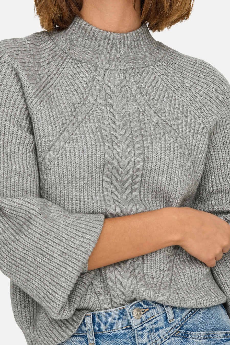 Pull à col roulé gris de ONLY®, avec motif torsadé et texture tricotée, porté avec un jean taille haute.
