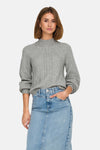 Pull à col roulé gris de ONLY, avec motif torsadé sur le devant, porté avec une jupe en jean.
