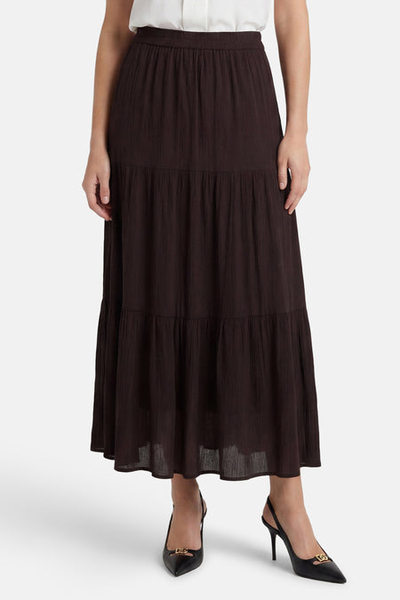 Jupe longue brune de ONLY® avec taille élastiquée, volants et texture froissée, portée avec un haut blanc et des escarpins noirs.