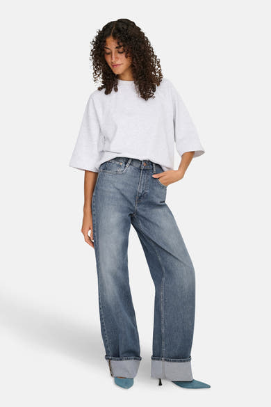 Wijde spijkerbroek in middieblauw denim van ONLY, gedragen met een lichtgrijs T-shirt en blauwe pumps.