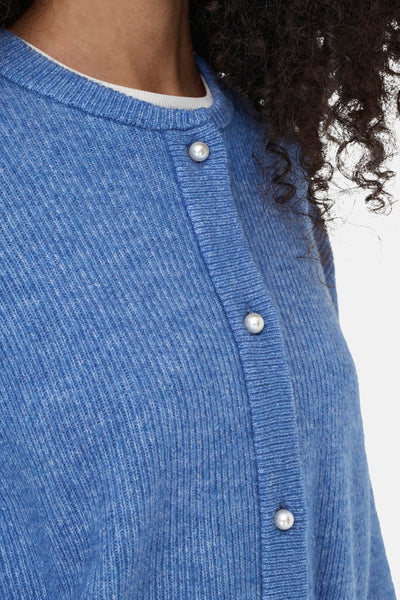 Cardigan bleu en maille par JDY, avec boutons décoratifs nacrés et encolure arrondie, porté sur un T-shirt blanc.