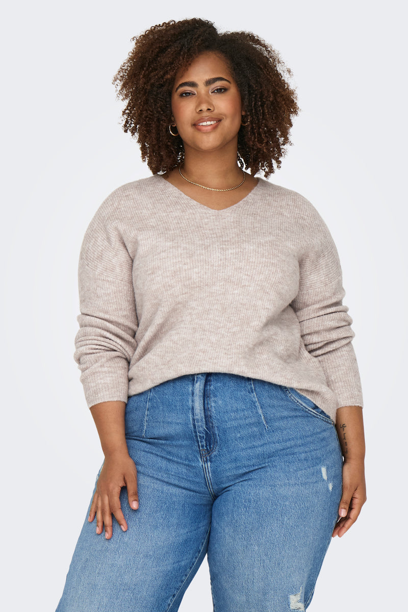 Pull à col en V beige de CARMAKOMA, porté avec un jean taille haute et un collier doré.
