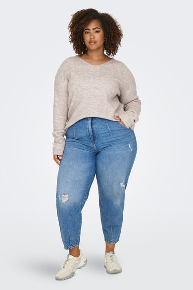 Pull à col en V beige de CARMAKOMA, porté avec un jean bleu ample et des baskets claires.
