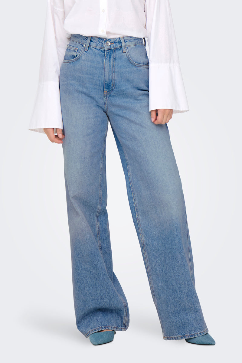 Jean large bleu moyen de ONLY, porté avec une chemise blanche à manches évasées et des escarpins bleus.