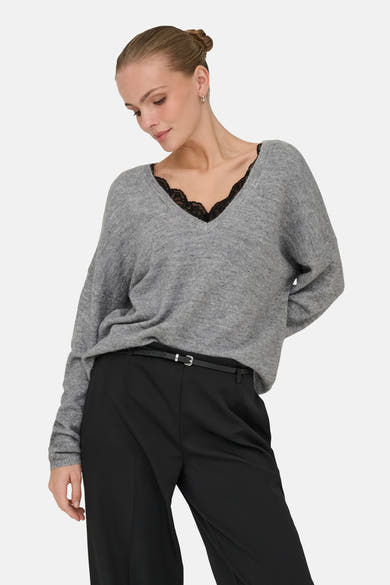 Grijze V-hals trui van ONLY, met zwart kanten detail bij de halslijn, gedragen met een zwarte broek en een dunne riem.