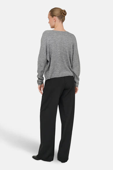 Grijze V-hals trui van ONLY, gedragen met een zwarte wijde broek en zwarte schoenen.