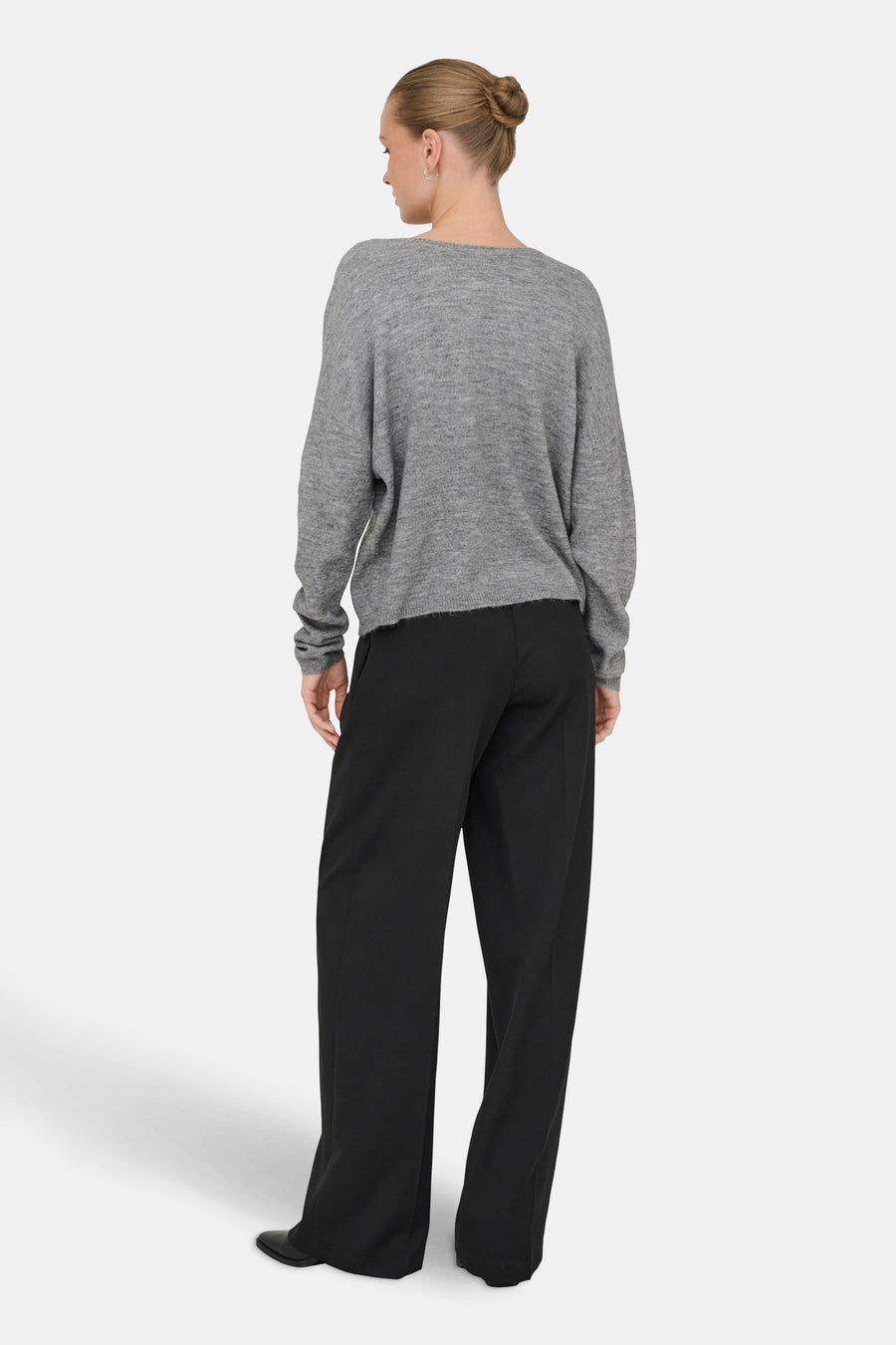 Grijze V-hals trui van ONLY, gedragen met een zwarte wijde broek en zwarte schoenen.