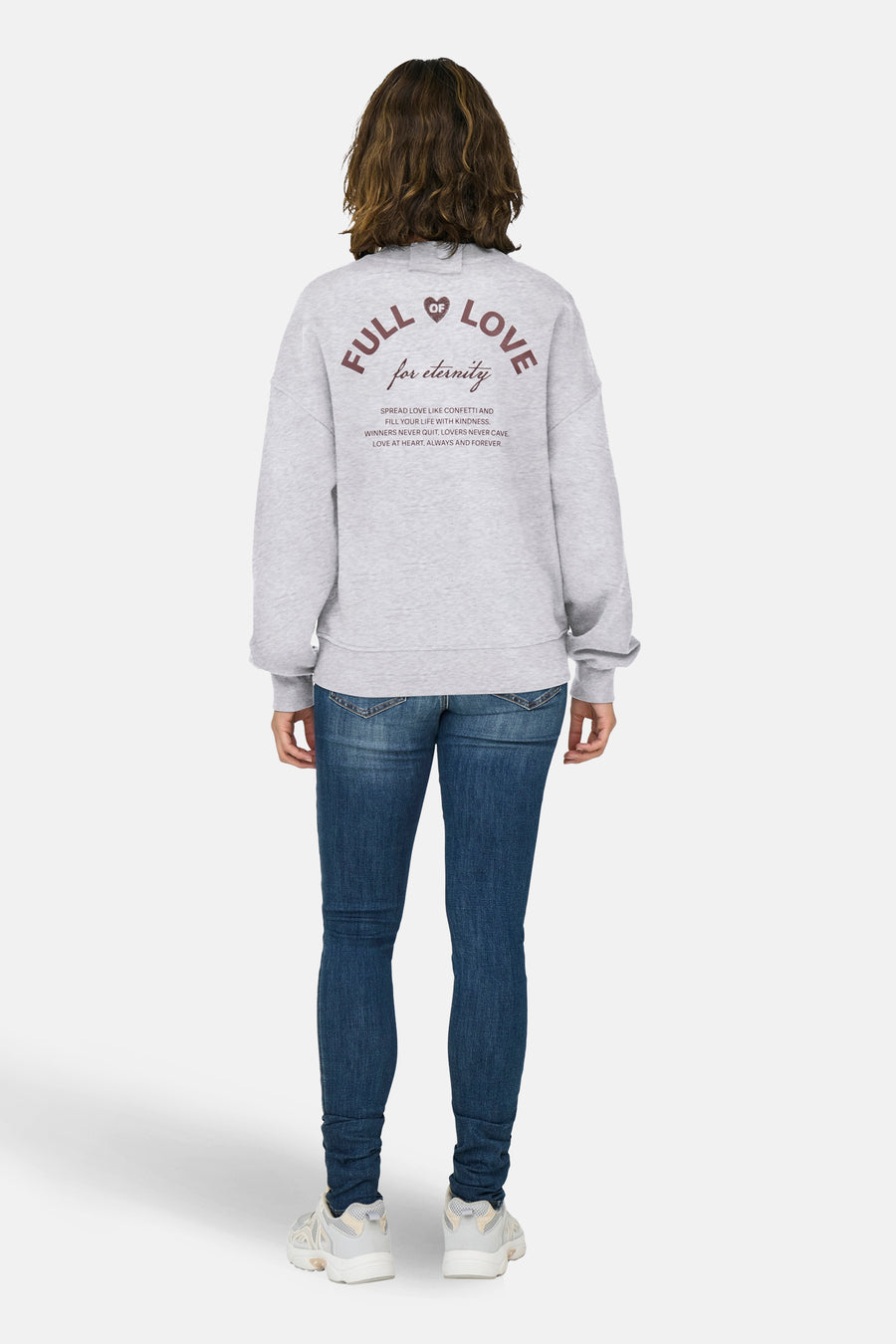 Sweat-shirt gris col rond de ONLY avec inscription décorative au dos, porté avec un jean bleu et des baskets.
