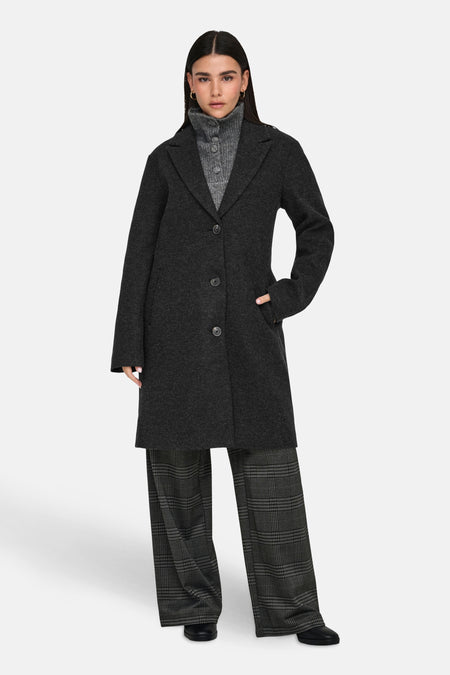 Zwarte lange jas van JDY, met knoopsluiting aan de voorkant, gedragen met geruite broek.