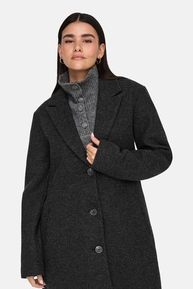 Veste longue noire de JDY, avec un col à revers et une doublure lisse, portée sur un pull à col roulé gris.
