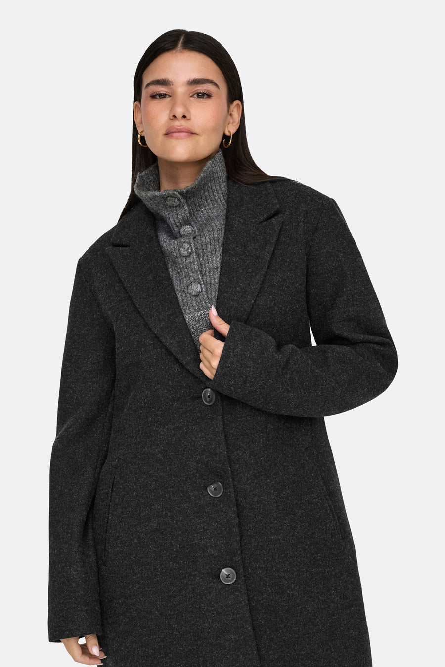 Veste longue noire de JDY, avec un col à revers et une doublure lisse, portée sur un pull à col roulé gris.
