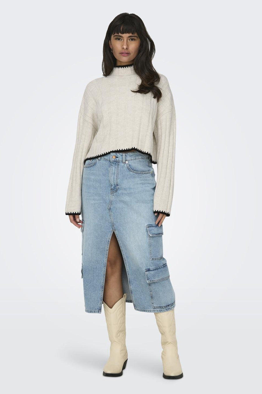 Pull à col roulé écru de ONLY, à texture côtelée, porté avec une jupe en jean à fente et des bottes blanches.
