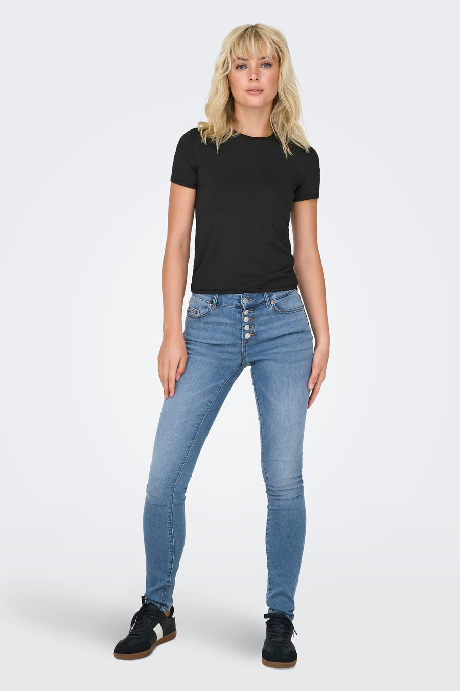 Zwarte top van ONLY, gedragen met een high-waisted jeans met knopen en zwarte sneakers.