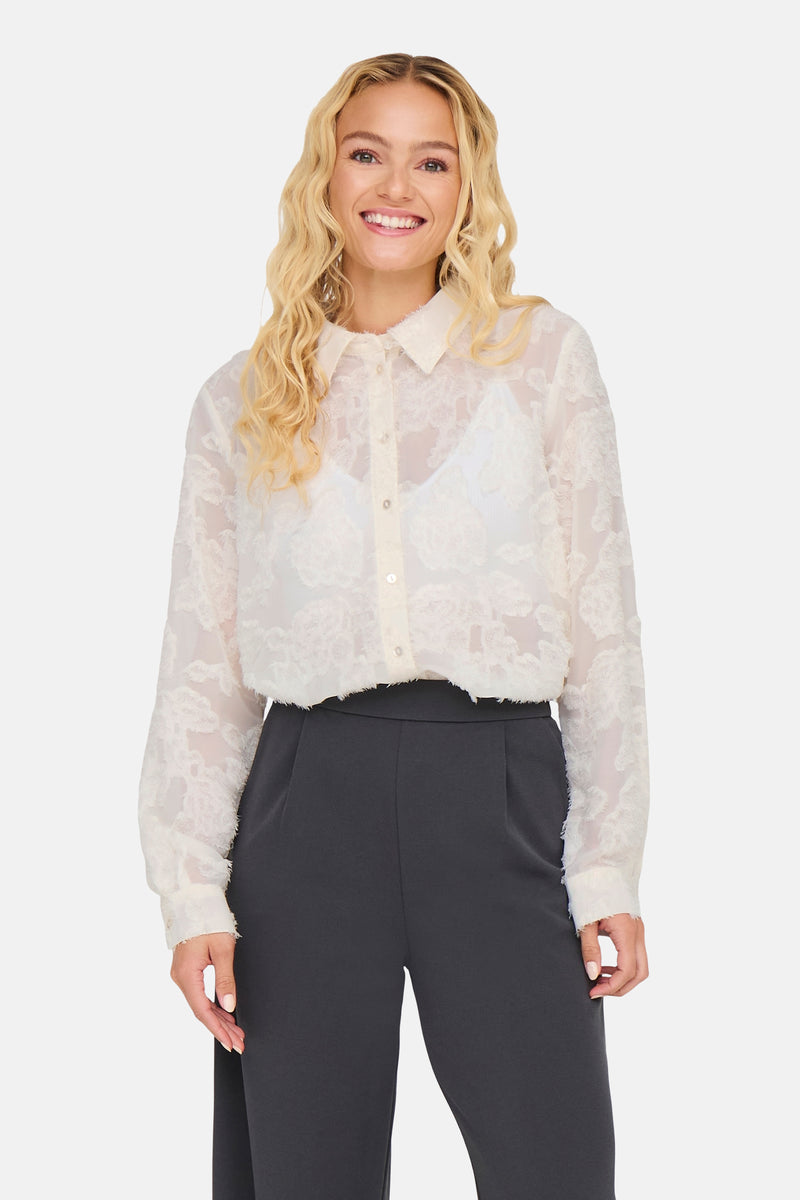 Chemise à manches longues blanche de JDY, à motifs floraux texturés, avec un soutien-gorge blanc visible.