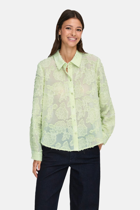 Chemise à manches longues verte de JDY, motif floral texturé, portée avec un jean sombre et des boucles d'oreilles.
