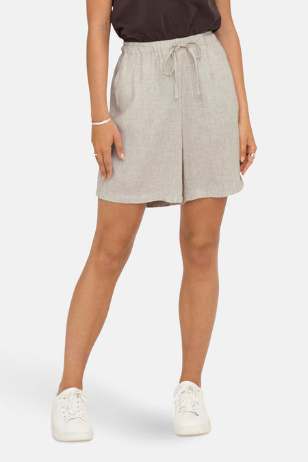 Short écru de ONLY, avec cordon de serrage et porté avec un bracelet et des chaussures blanches.
