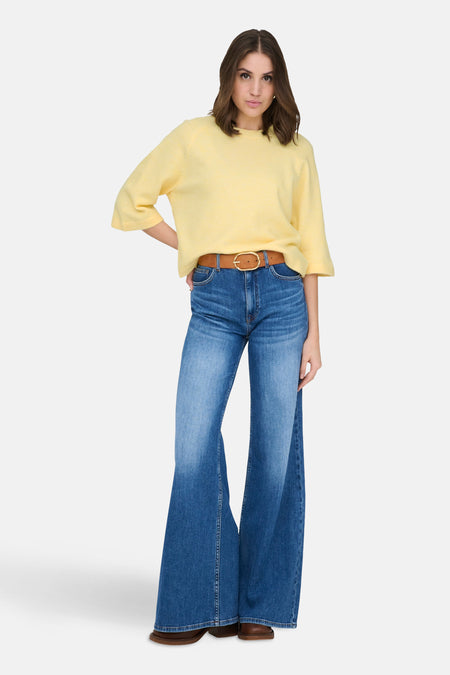 Pull à col rond jaune de ONLY, porté avec un pantalon évasé en denim bleu et une ceinture marron.