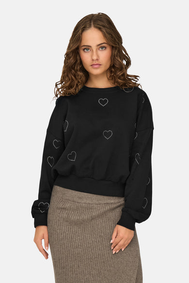 Sweat noir à col rond par ONLY orné de motifs de coeurs argentés, porté avec une jupe côtelée marron.
